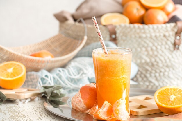 Świeżo uprawiany ekologiczny świeży sok pomarańczowy we wnętrzu domu, turkusowy koc i kosz owoców
