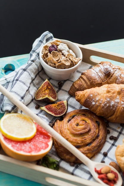 Świeży croissant; słodkie wypieki; płatki kukurydziane; owoce figowe i cytrusowe podawane na śniadanie na tacy