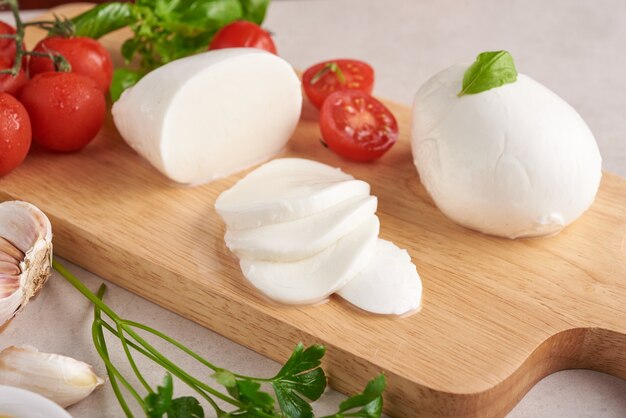 Świeży ser mozzarella, miękkie włoskie sery, pomidor i bazylia, oliwa z oliwek i rozmaryn na drewnianej desce do serwowania na jasnej drewnianej powierzchni. Zdrowe jedzenie. Widok z góry. Leżał na płasko.