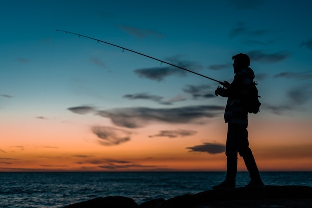 Sylwetka człowieka, łowienie ryb na plaży o zachodzie słońca