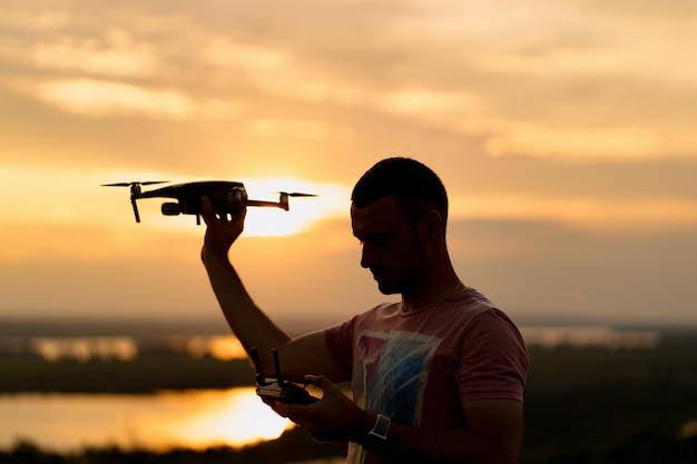 Sylwetka człowieka pilotującego drona o zachodzie słońca ze słonecznym niebem w tle