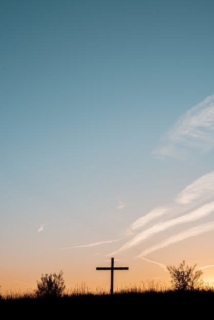 Bezpłatne zdjęcie sylwetka drewniany krzyż na trawiastym wzgórzu z pięknym niebem