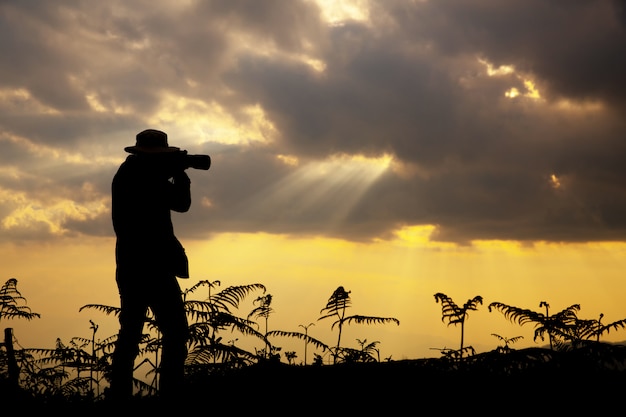 sylwetka fotografa, który fotografuje zachód słońca w górach