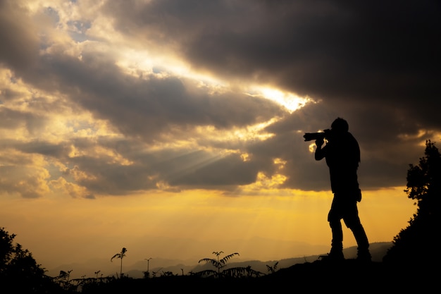 sylwetka fotografa, który fotografuje zachód słońca w górach