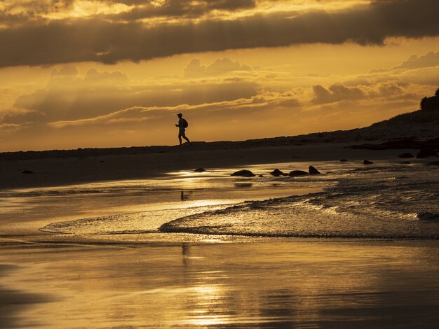 Sylwetka mężczyzny biegnącego na skalistym brzegu morza pod złotym niebem słońca