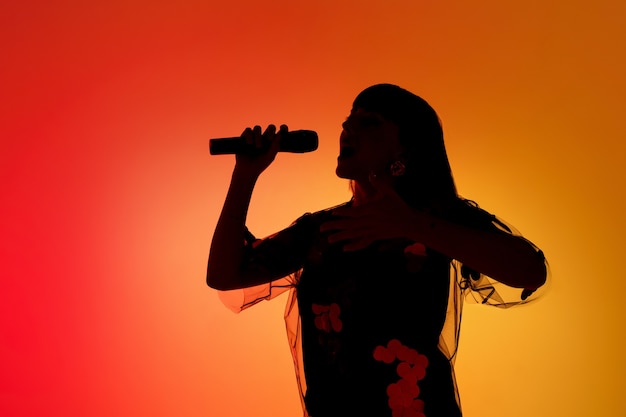 Sylwetka młodej kaukaskiej piosenkarki odizolowanej na pomarańczowym tle gradientu studio w neonowym