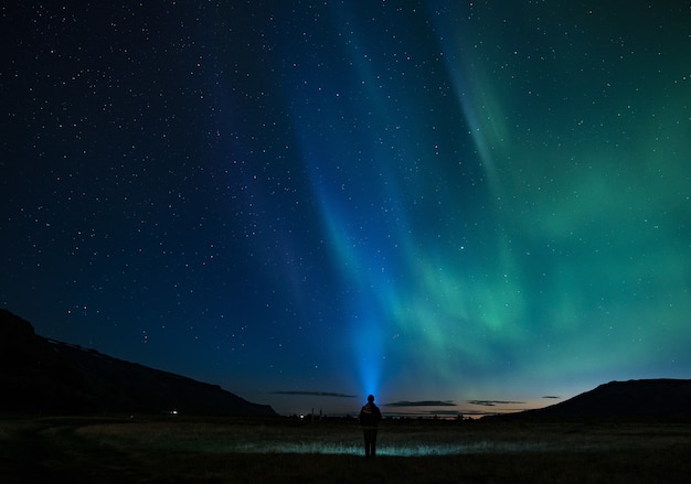 Sylwetka osoby stojącej pod nocnym niebem aurora