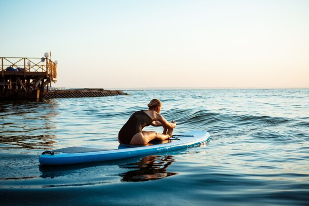 Sylwetka pięknej kobiety ćwiczy joga na surfboard przy wschodem słońca.