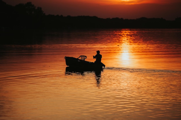 Sylwetka rybaka nad jeziorem podczas zachodu słońca