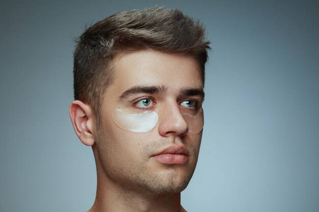 Szczegół portret profil młodego człowieka na białym tle na szarym tle. Męska twarz z kolagenowymi plamami pod oczami.