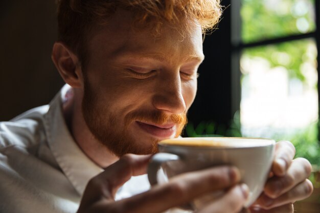 Szczegół portret wesoły rudy brodaty mężczyzna wącha kawę z zamkniętymi oczami