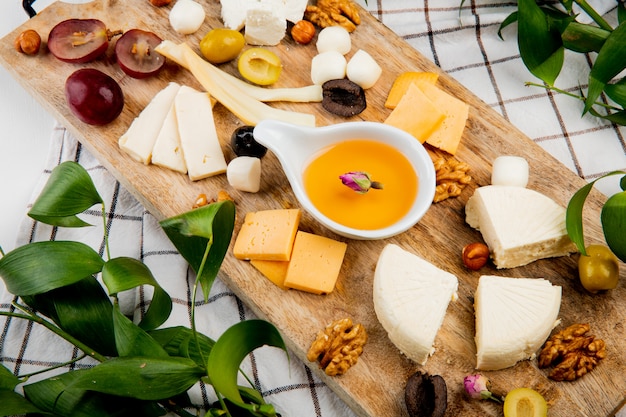 Szczegół widok roztopionego masła z różnego rodzaju sera winogronowego kawałki oliwek orzechów na desce do krojenia na kratę ozdobiony liśćmi