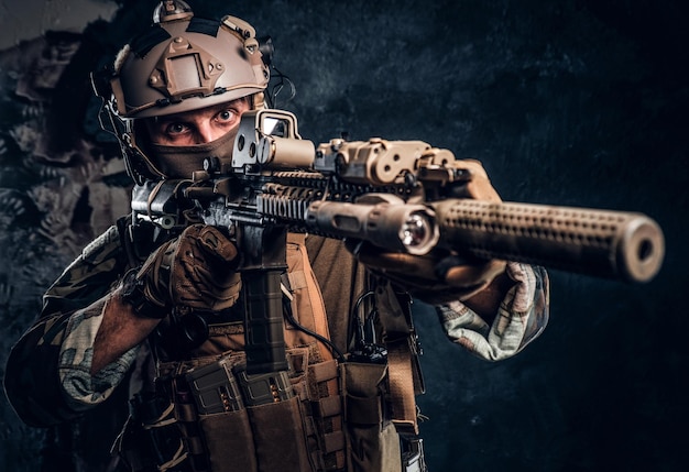 Szczegółowa fotografia studyjna. Elitarna jednostka, żołnierz sił specjalnych w mundurze kamuflażowym, trzymający karabin szturmowy z celownikiem laserowym i celujący w cel.