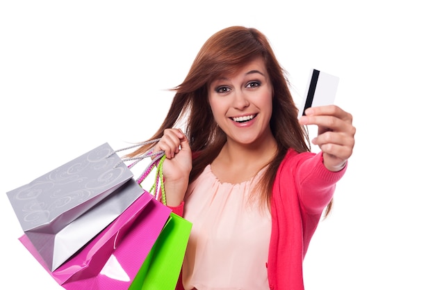 Szczery młoda kobieta pokazuje kartę kredytową i trzyma torby na zakupy