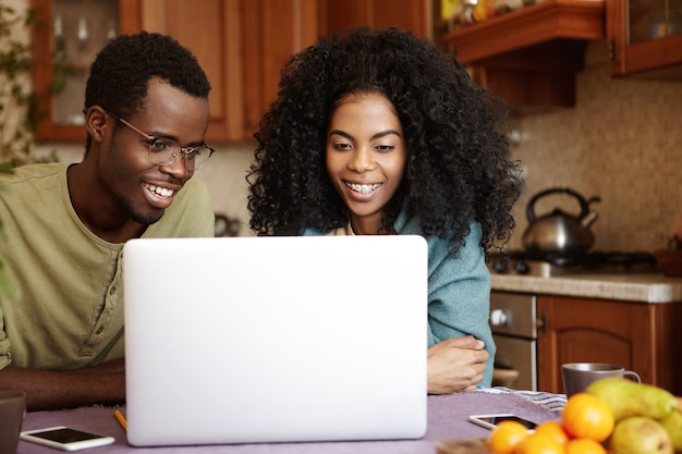 Szczery strzał pięknej młodej pary African-American siedzi przy stole w kuchni przed otwartym laptopem