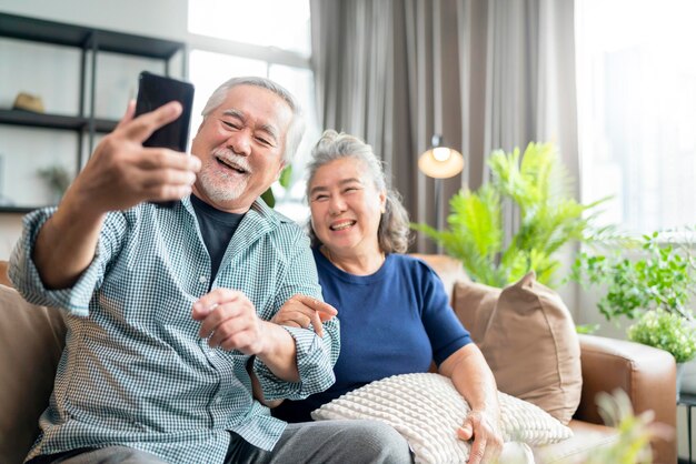 Szczęście azjatycka starsza para emerytów cieszy się połączeniem wideo z rodziną razem na kanapie w salonie w homeasian ludzie używają komunikacji smartfona do koncepcji izolacji domu rodzinnego