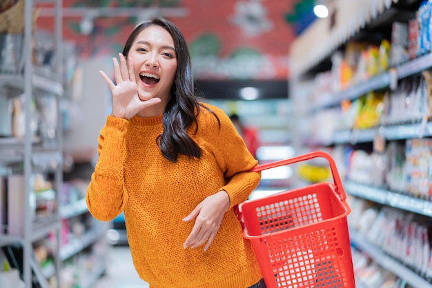 Szczęście wesoły odeszła azjatycka kobieta dorywczo szmatka trzymaj za rękę pusty koszyk na zakupy gest dłoni ogłaszaj dobre wieści lub nową promocję do kamery azjatycka kobieta uśmiechająca się w supermarkecie spożywczym