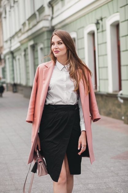 Szczęśliwa atrakcyjna stylowa uśmiechnięta kobieta spaceru ulicą miasta w trend w modzie wiosna różowy płaszcz, elegancki styl