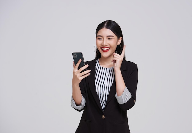 Szczęśliwa azjatycka bizneswoman w garniturze używająca telefonu do komunikacji odizolowana na szarym tle
