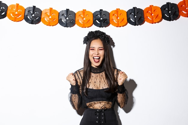 Szczęśliwa Azjatycka Kobieta Korzystająca Z Halloween, Ubrana W Kostium Złej Wiedźmy I Radująca Się Z Dekoracji Dyniowych Serpentyn.