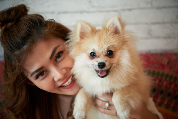 Szczęśliwa Azjatycka kobieta pozuje z małym zwierzę domowe psem w domu