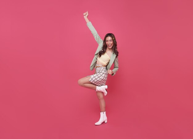 Szczęśliwa Azjatycka kobieta uśmiecha się i skacze, świętując sukces na białym tle na różowym tle