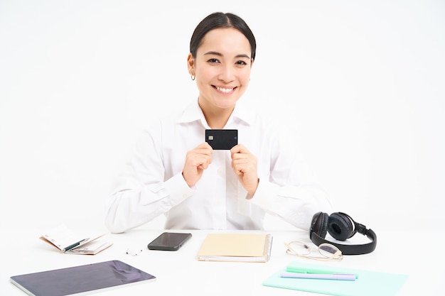 Szczęśliwa bizneswoman siedzi w biurze pokazuje kartę kredytową i uśmiecha się, płaci zbliżeniowo, czekając na wypłatę