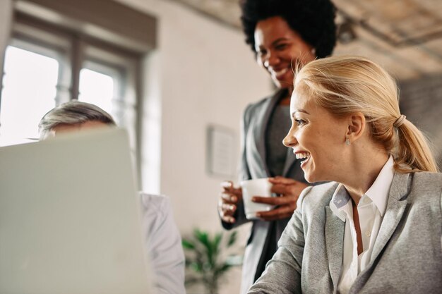 Szczęśliwa bizneswoman w średnim wieku rozmawia ze swoimi współpracownikami i śmieje się podczas pracy w biurze