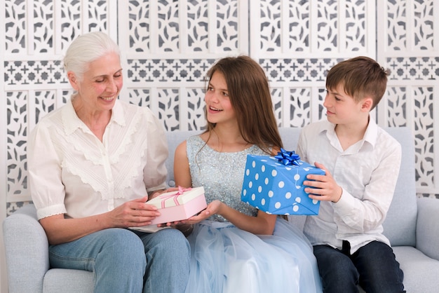 Szczęśliwa chłopiec i dziewczyna daje prezentów pudełkom ich babcia przy przyjęciem urodzinowym