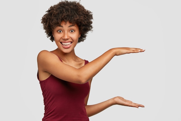 Szczęśliwa czarna młoda kobieta z zadowolonym wyrazem twarzy pokazuje wysokość czegoś
