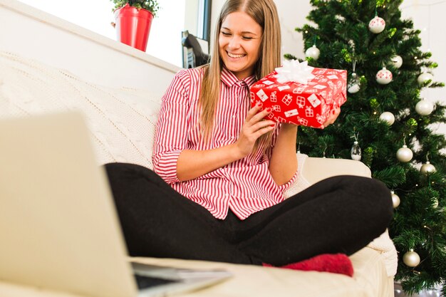 Szczęśliwa dama z prezenta pudełkiem blisko laptopu i choinki