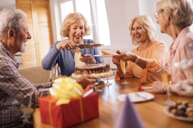 Szczęśliwa dojrzała kobieta świętująca urodziny z przyjaciółmi i serwująca im ciasto w domu
