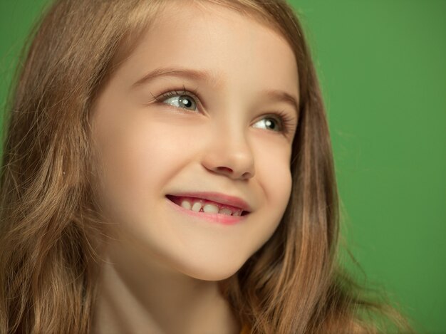 Szczęśliwa dziewczyna stojąc, uśmiechając się na białym tle na modnym zielonym tle studio. Piękny portret kobiety. Młoda dziewczyna zadowoli. Ludzkie emocje, koncepcja wyrazu twarzy. Przedni widok.