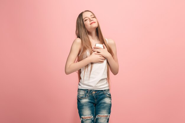 Szczęśliwa dziewczyna stojąc, uśmiechając się z telefonu komórkowego na modnym różowym tle studio. Piękny portret kobiety w połowie długości. Ludzkie emocje, koncepcja wyrazu twarzy.