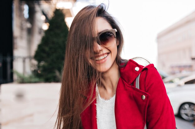 Szczęśliwa dziewczyna w duże okulary przeciwsłoneczne wyrażające enegry podczas ulicznej sesji zdjęciowej