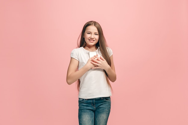 Bezpłatne zdjęcie szczęśliwa dziewczyna z telefonem stojąc i uśmiechając się przed różową ścianą