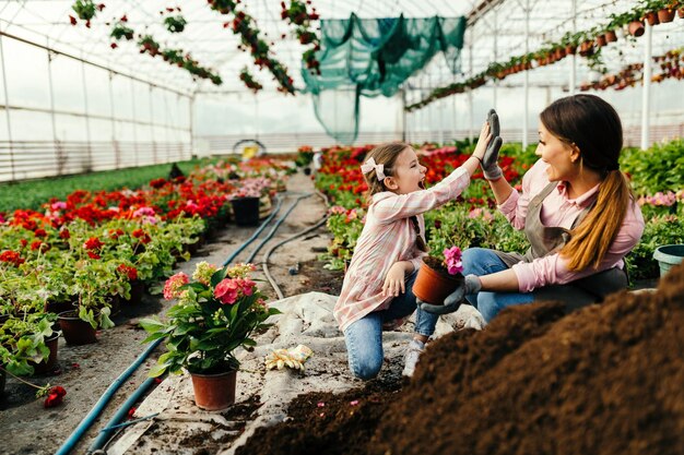 Szczęśliwa dziewczynka i jej mama przybijają sobie nawzajem piątkę podczas sadzenia kwiatów w szkółce roślin