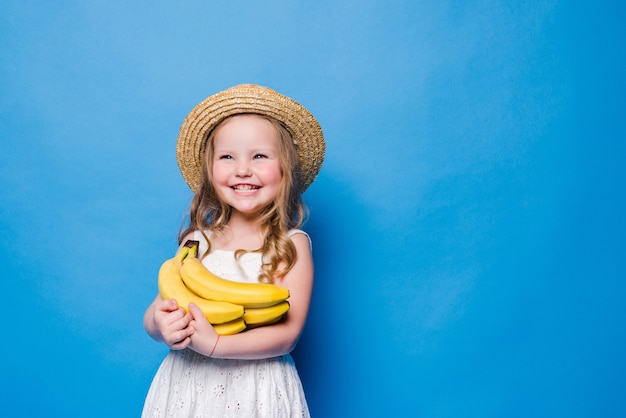 Szczęśliwa dziewczynka z żółtymi bananami na białym tle na niebieskiej ścianie