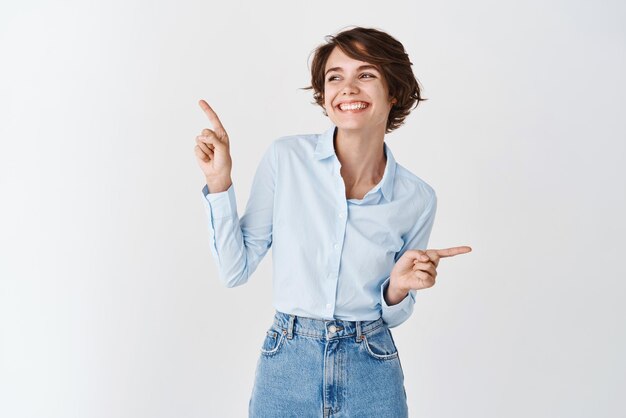 Szczęśliwa europejska kobieta w profesjonalnej odzieży biurowej wskazując palcami na boki, uśmiechnięta i patrząca w lewo, dokonująca wyboru stojącego na białym tle