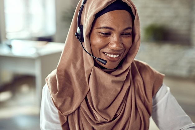 Szczęśliwa islamska bizneswoman nosząca zestaw słuchawkowy podczas pracy w biurze