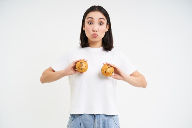 Szczęśliwa Japonka Pokazuje Babeczki Na Klatce Piersiowej Jedząc Ciasto Stojące Nad Białym Tłem
