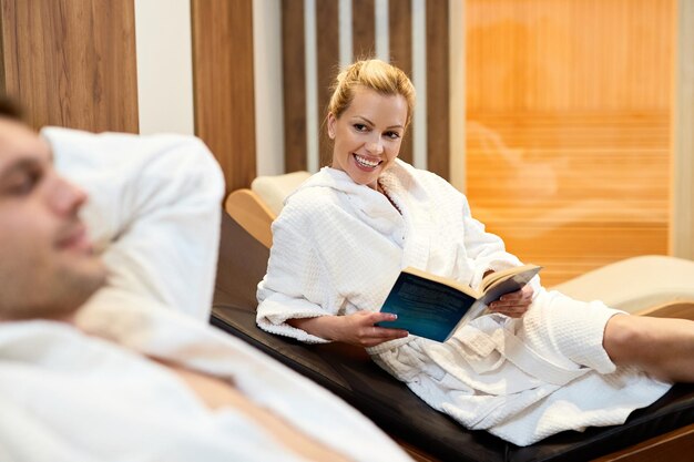 Szczęśliwa kobieta czytająca książkę podczas relaksującego dnia z mężem w centrum odnowy biologicznej