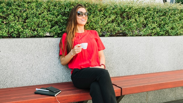 Bezpłatne zdjęcie szczęśliwa kobieta jest ubranym okulary przeciwsłonecznych pije kawę