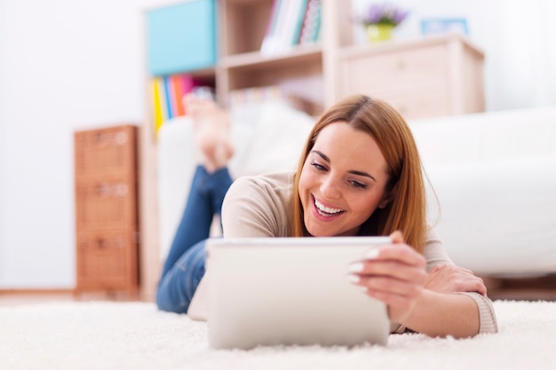 Szczęśliwa kobieta leżąc na dywanie z cyfrowego tabletu