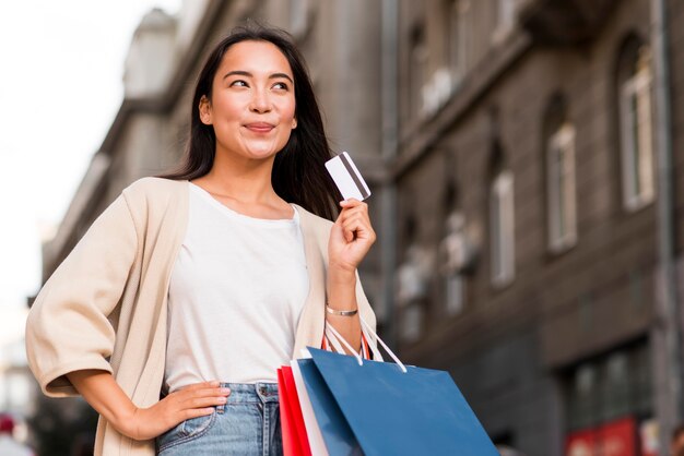 Szczęśliwa kobieta na zewnątrz trzymając torby na zakupy i kartę kredytową