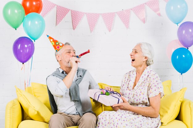 Szczęśliwa kobieta patrzeje jej męża dmuchania przyjęcia róg z prezentem urodzinowym