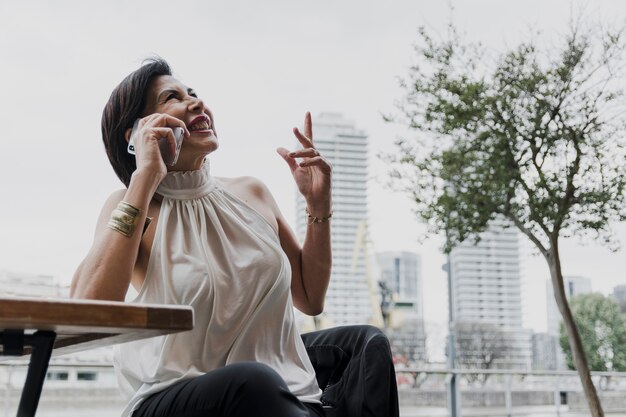 Szczęśliwa kobieta trzyma telefon na miasta tle