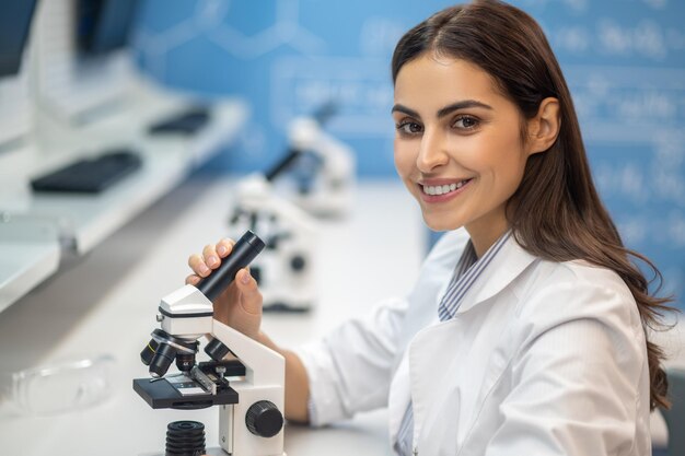 Szczęśliwa kobieta w pobliżu mikroskopu patrząc na kamerę