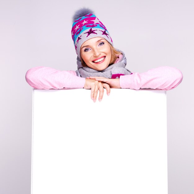 Bezpłatne zdjęcie szczęśliwa kobieta w zimowej odzieży wierzchniej na biały afisz w rękach