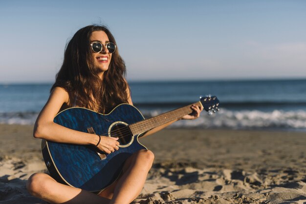 Szczęśliwa kobieta z gitarą na plaży